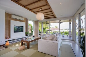 Una sala de estar moderna con un televisor de pantalla plana, techo de madera y ventanas amplias.