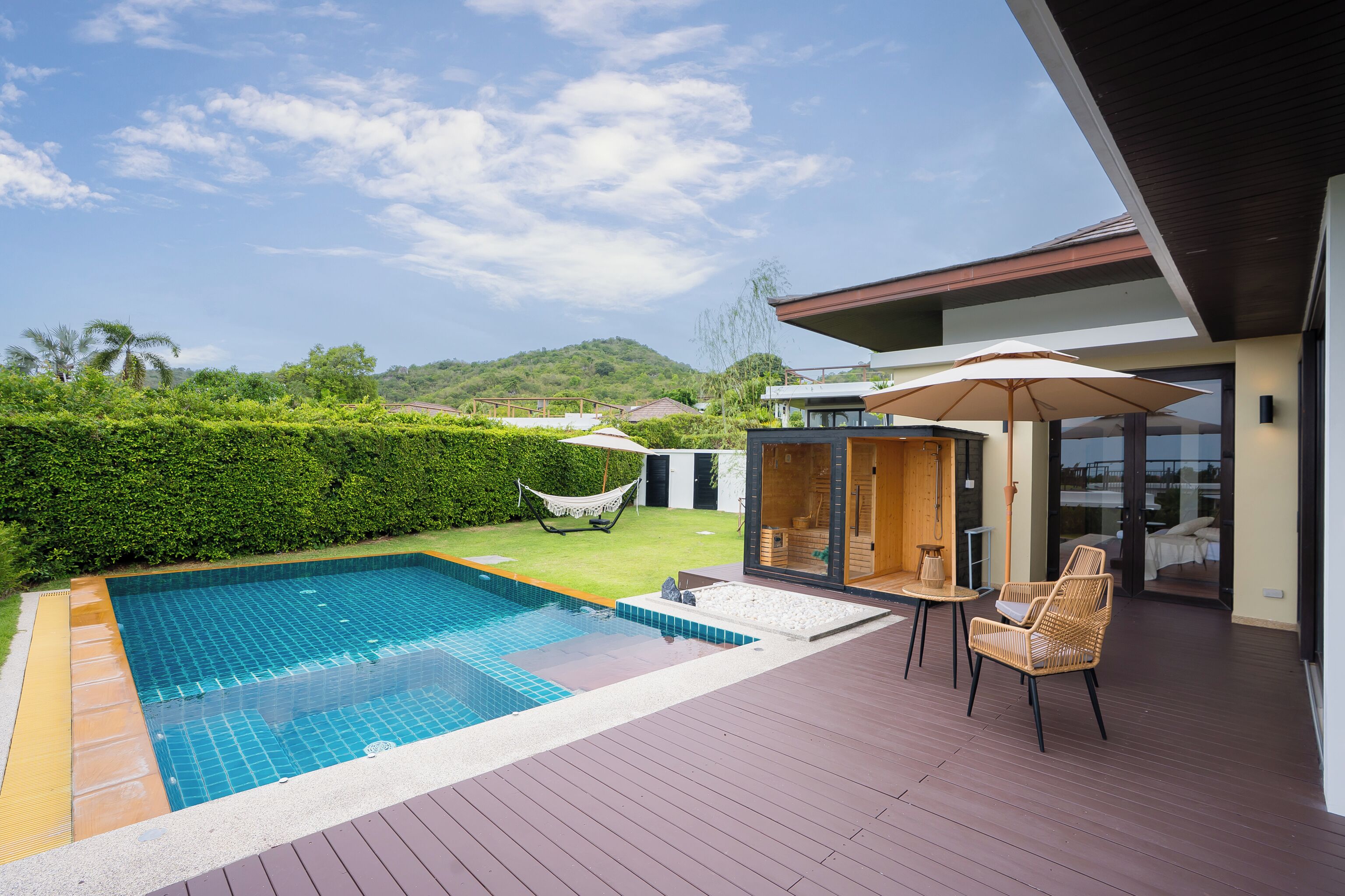 Une piscine avec une terrasse en bois, du mobilier d’extérieur et une vue sur une colline.