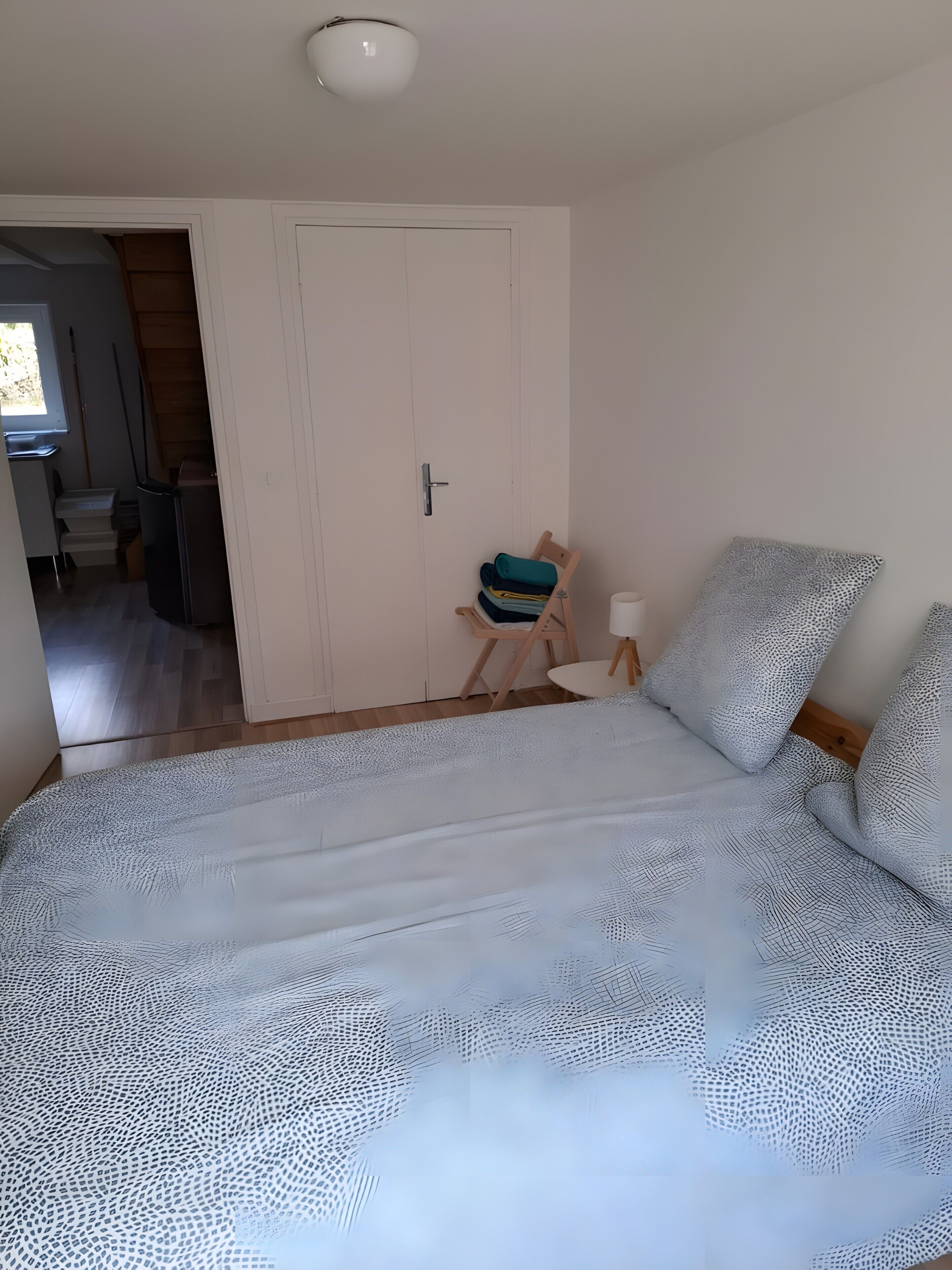 A bedroom with a bed, a chair, a door, and a small table.