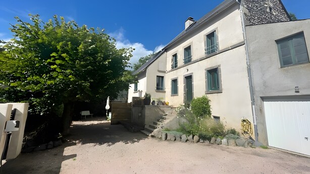 A two-story building with a sloped roof, a staircase leading to the entrance, and a white garage door. - Le Puy d’Eraigne: peaceful, cool apartment with terrace and optional garage on request (Saint-Nectaire)
