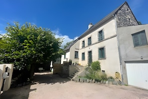 A two-story building with a sloped roof, a staircase leading to the entrance, and a white garage door. - Le Puy d’Eraigne: peaceful, cool apartment with terrace and optional garage on request (Saint-Nectaire)