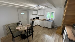 A modern kitchen with white cabinetry, a dining area with a table and chairs, and a view of greenery through a window. - Le Puy d’Eraigne: peaceful, cool apartment with terrace and optional garage on request (Saint-Nectaire)