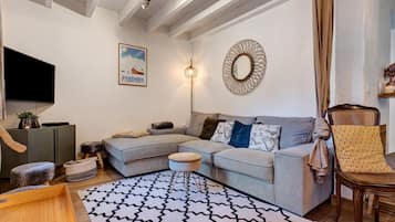 Een moderne woonkamer met een grijze modulaire bank, een getextureerd vloerkleed, een houten salontafel, een rieten fauteuil en een flatscreen tv aan de muur.