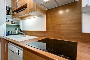 A modern kitchen with a Bosch dishwasher, a black induction cooktop, wooden cabinets, and a white countertop.