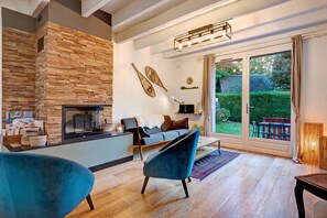 A modern living room with a stone fireplace, a sofa, and a large window overlooking a garden.