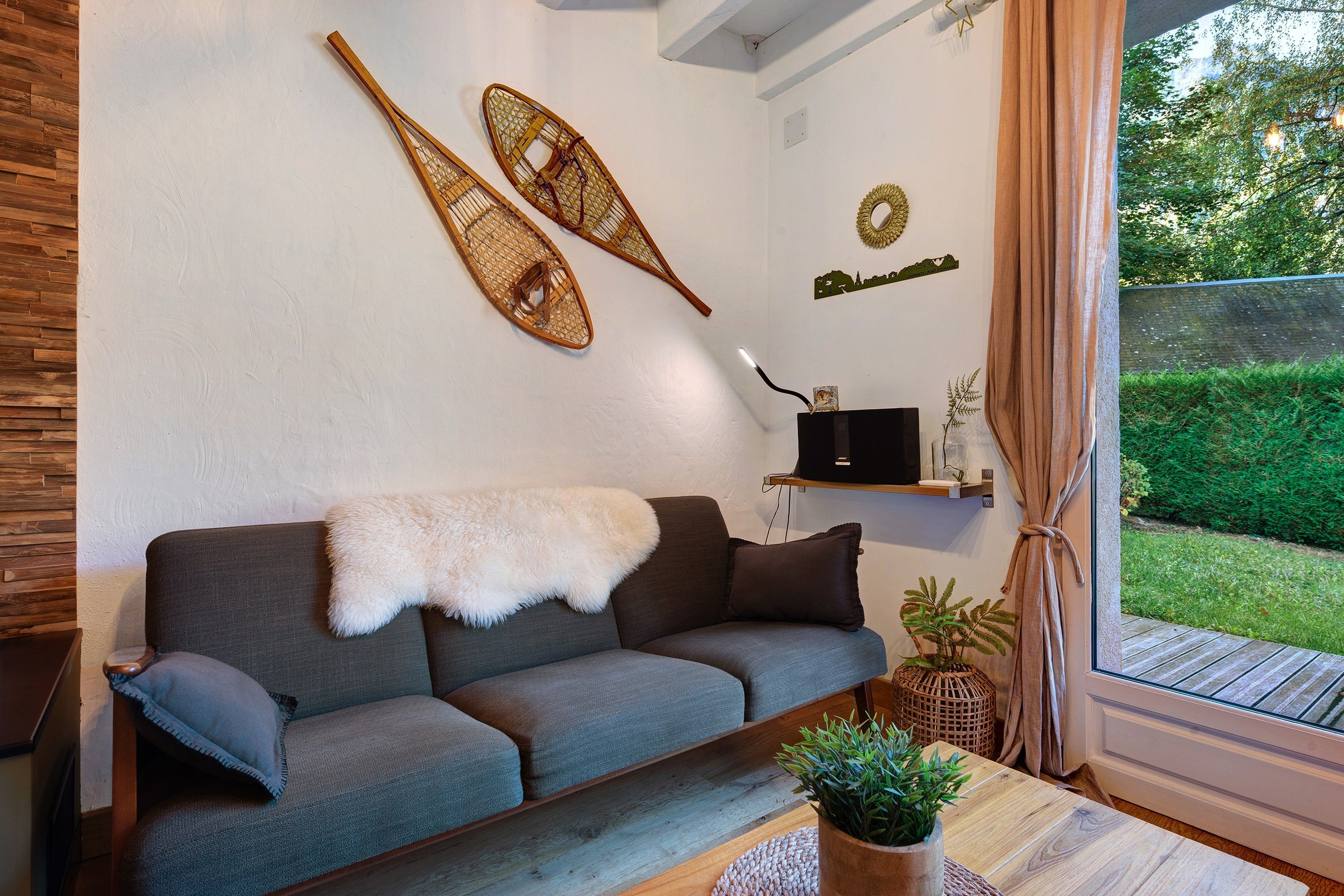 Una sala de estar moderna con un sofá gris, un plaid blanco suave y una mesa de centro de madera con una planta.