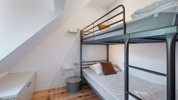Habitación con literas, un escritorio pequeño y un cubo de basura.