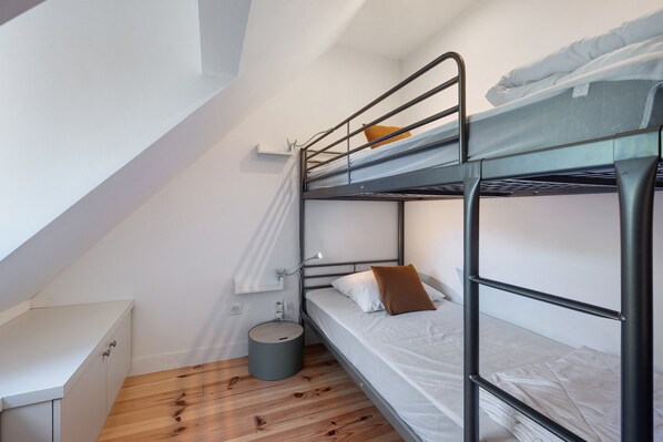Une chambre avec un lit superposé, un petit bureau et une poubelle.