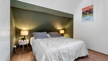 Een slaapkamer met een bed, twee bedlampen, een nachtkastje, een aan de muur hangend schilderij en een houten vloer.