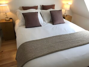 A neatly made bed with a patterned throw, two bedside lamps, and a wooden nightstand.