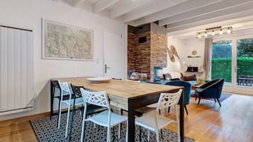 Een eetgedeelte met een houten tafel en stoelen, een keuken met een stenen muur, en uitzicht op een tuin door een glazen deur.