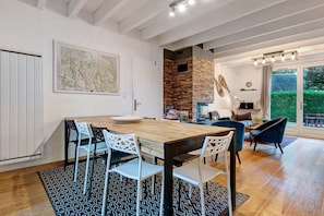 Un coin repas avec une table et des chaises en bois, une cuisine avec un mur en pierre et une vue sur un jardin, visible à travers une porte vitrée.