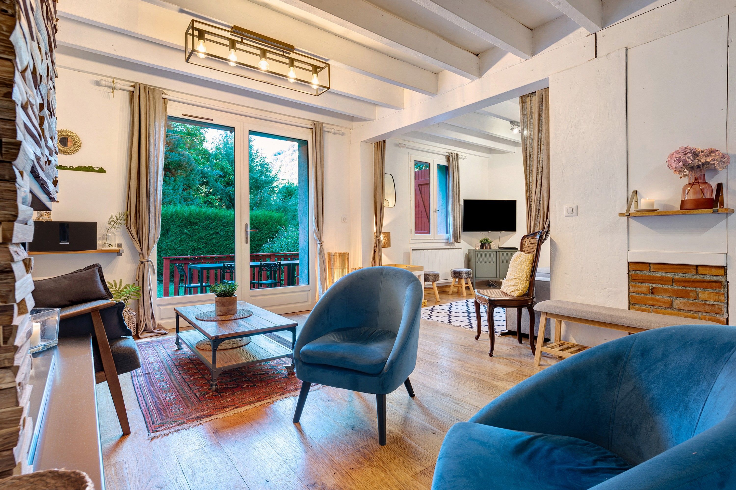 Un salon spacieux avec une grande fenêtre, un fauteuil bleu, une table basse en bois et un téléviseur.