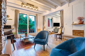 Un salon spacieux avec une grande fenêtre, un fauteuil bleu, une table basse en bois et un téléviseur.