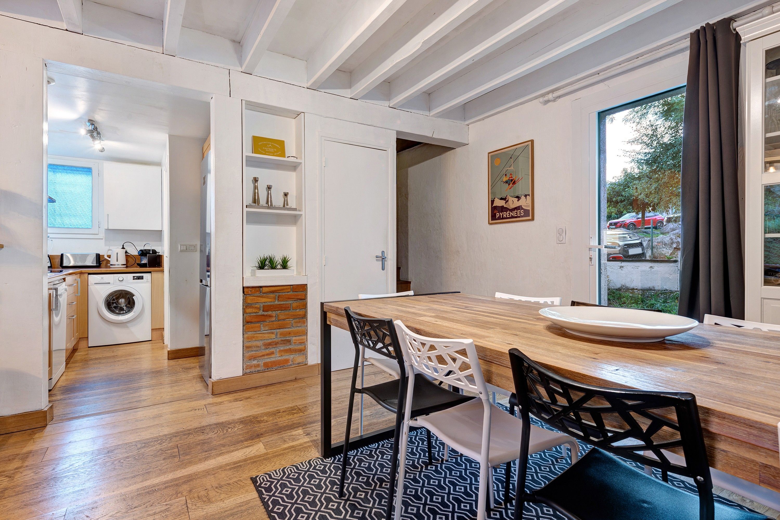 Une cuisine moderne avec des meubles blancs, un lave-linge et un coin repas comprenant une table et des chaises en bois.