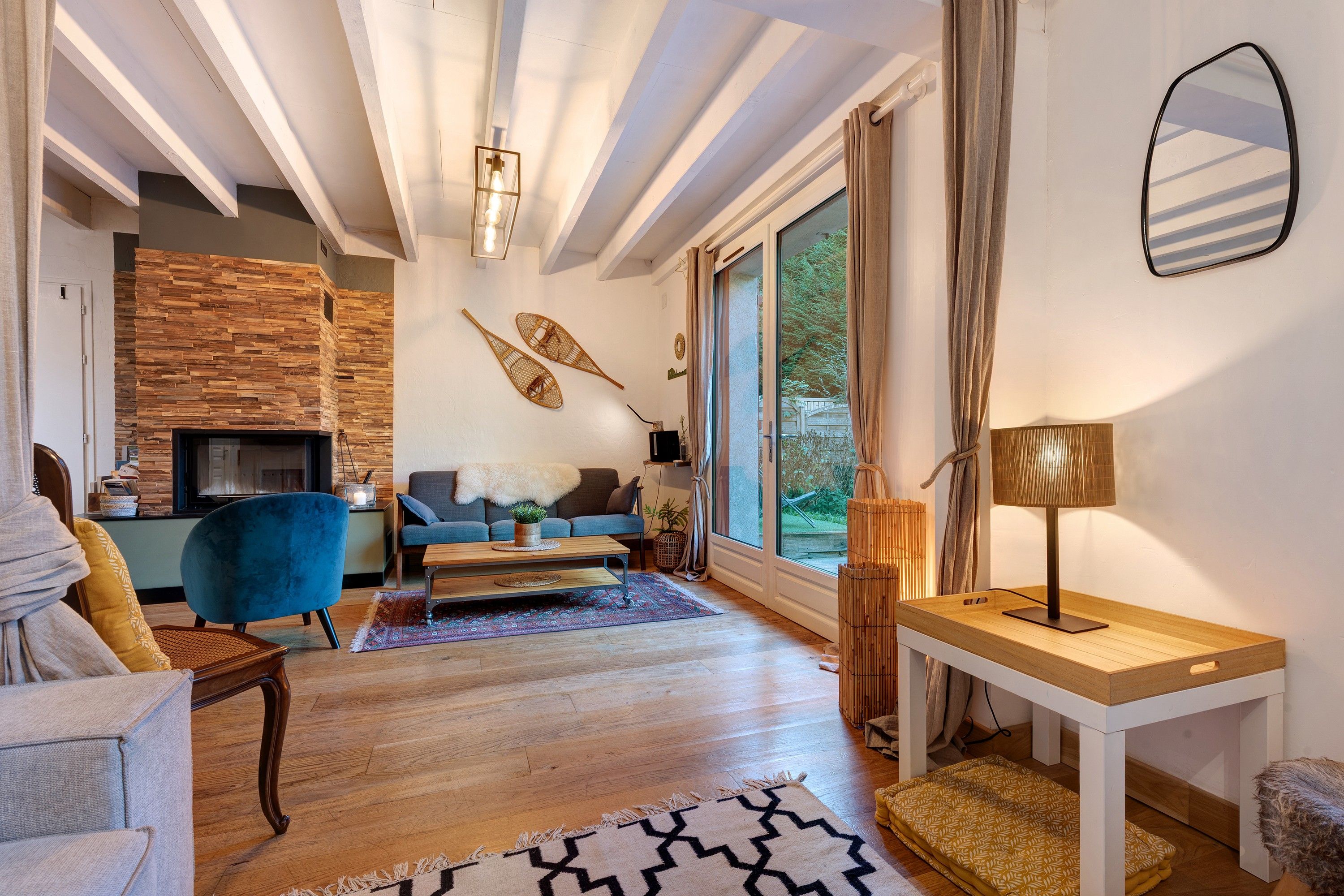 Una sala de estar moderna con chimenea, un sofá, un sillón azul y una mesa con lámpara.