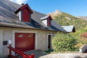 Un bâtiment à deux étages, avec une porte et des fenêtres rouges, se dressant sur fond de paysage montagneux.