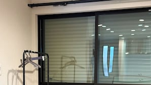 Ein Zimmer mit Fenster, einem Holztisch und einem Metallregal.