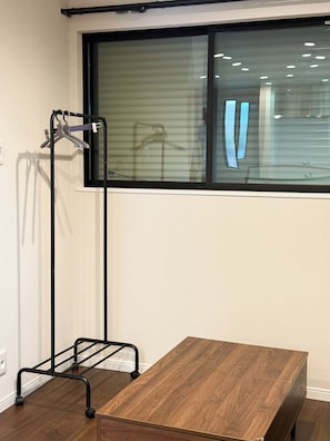 Ein Zimmer mit Fenster, einem Holztisch und einem Metallregal.