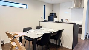 Ein moderner Essbereich mit einem Tisch für vier Personen, schwarzen Stühlen, einem Holzstuhl, einer Küche mit Mikrowelle und einer Edelstahl-Dunstabzugshaube.
