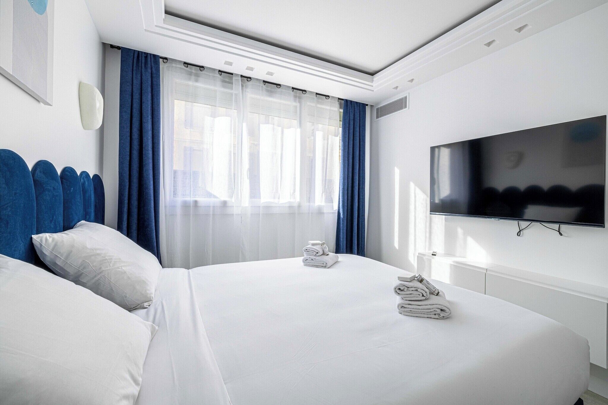 A hotel room with two beds, a flat-screen TV, and a large window with curtains.