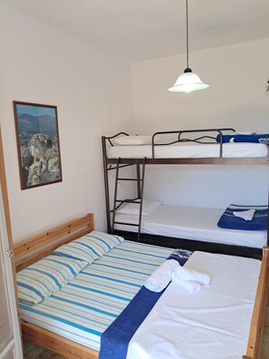 Ein Schlafraum mit Etagenbett und Leiter, einem Einzelbett mit gestreifter Bettwäsche, einer Pendelleuchte und einem gerahmten Bild an der Wand.