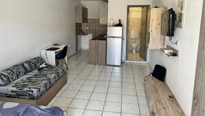Um espaço compacto com sofá, pequena cozinha, sanita e televisão fixada na parede.
