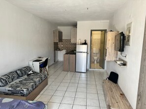Ein kompakter Wohnbereich mit Sofa, einer kleinen Küchenzeile, Toilette und einem an der Wand befestigten Fernseher.