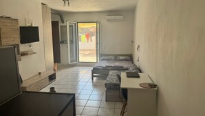 Quarto compacto com cama, escrivaninha, televisão e porta de correr para área externa.