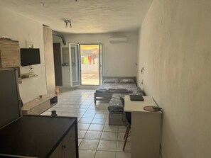 Ein kleines Zimmer mit Bett, Schreibtisch, Fernseher und einer Schiebetür zu einem Außenbereich.