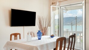 A dining area with a table, chairs, a TV, and a view of the sea through a glass door.