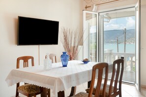 Een eetgedeelte met een tafel, stoelen, een televisie en uitzicht op zee door een glazen deur.