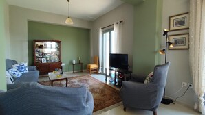 Una sala de estar con televisor, dos sillones, un aparador de madera y una mesa de comedor.