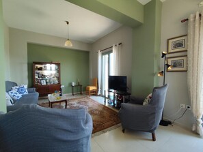 Ein Wohnzimmer mit Fernseher, zwei Sesseln, einem Holzschrank und einem Esstisch.
