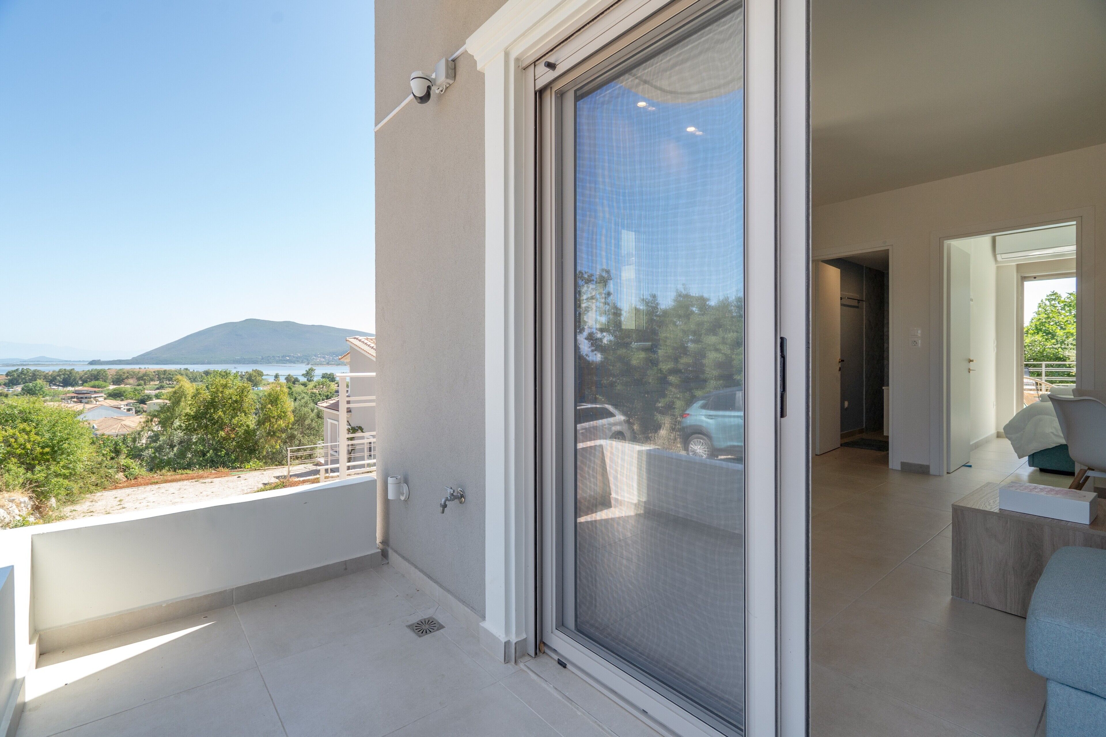 Un balcon avec vue sur une montagne et un plan d’eau, une porte-fenêtre coulissante et un intérieur moderne comprenant un canapé et une table basse.