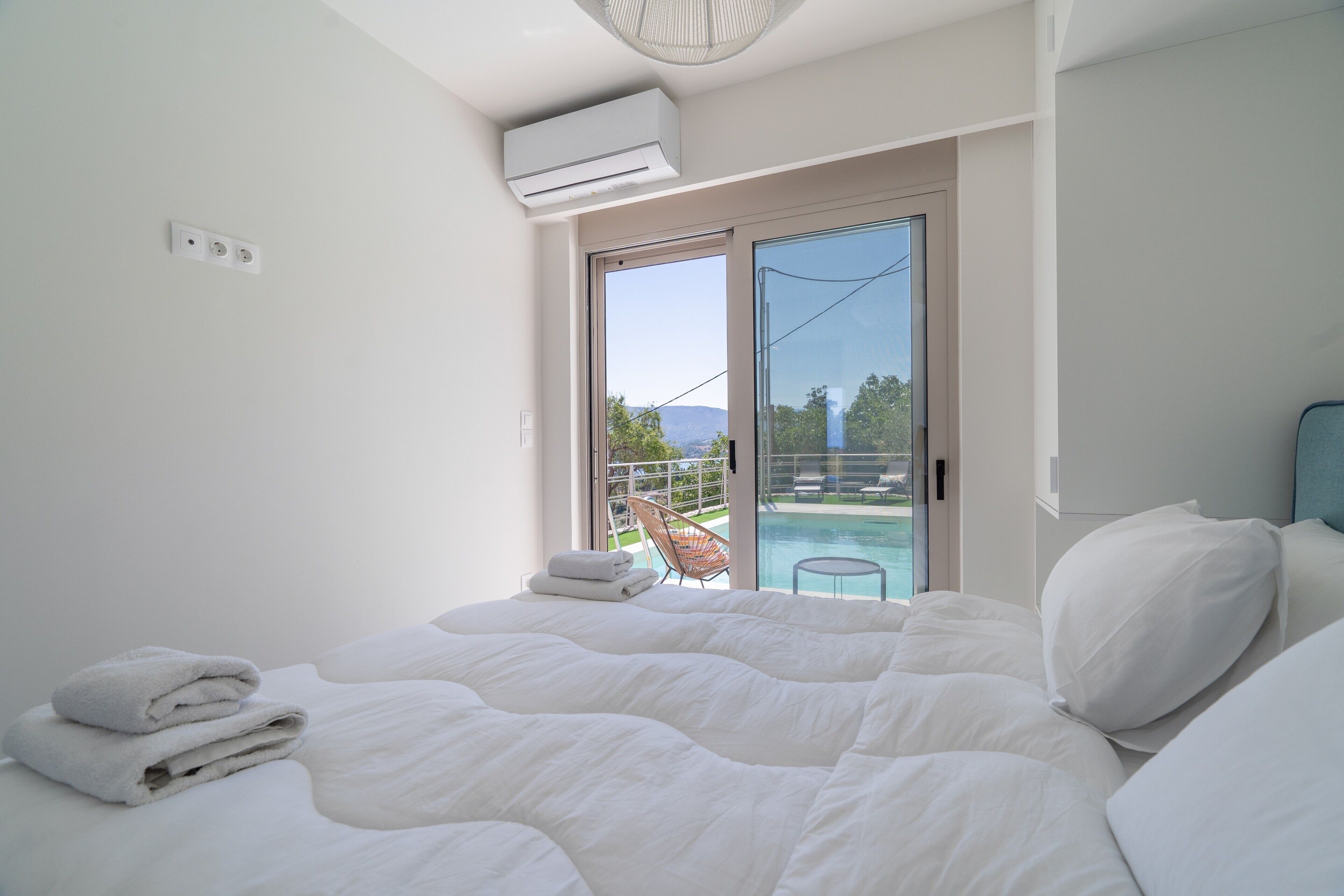 A bedroom with a bed, a chair, a balcony, and a pool view.