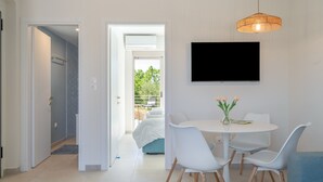 Un intérieur moderne comprenant un coin repas, un téléviseur fixé au mur et une vue sur un balcon, accessible par une porte ouverte.