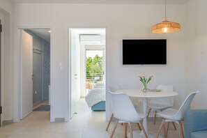Un interno moderno con zona pranzo, televisore montato a parete e vista su un balcone attraverso una porta aperta.