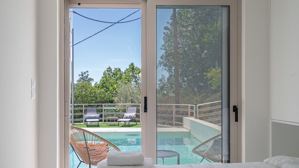 Une chambre avec un grand lit et une porte vitrée donnant sur un espace piscine équipé de chaises longues.