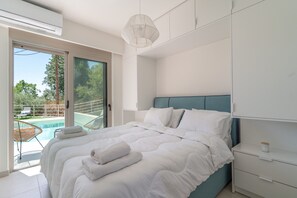 Ein Schlafzimmer mit Bett, Nachttisch, Deckenleuchte und Blick auf einen Pool.