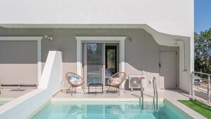 Un bâtiment moderne doté d’une piscine, de deux fauteuils en osier, d’une porte-fenêtre coulissante et d’une porte de garage blanche.