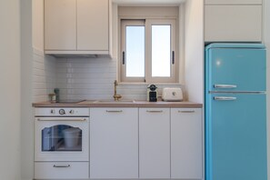 Eine Küche mit weißen Schränken, einem blauen Kühlschrank, einem Fenster und einem eingebauten Backofen.