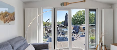 A modern living room with a grey sofa, a glass coffee table, and a view of an outdoor deck with outdoor furniture.