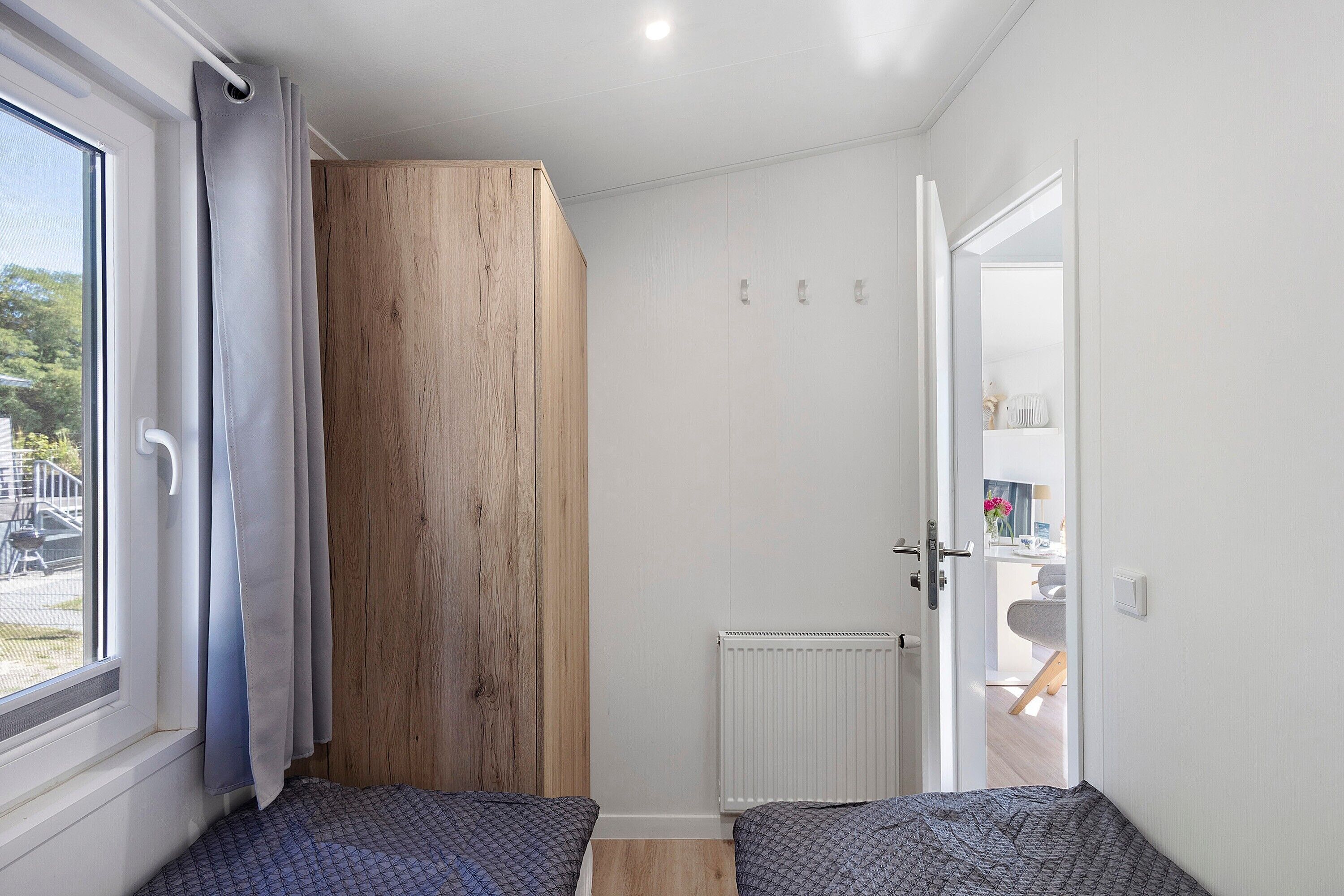Ein Zimmer mit einem großen Fenster, einem Heizkörper und einer Tür zu einem anderen Raum.