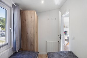 Ein Zimmer mit einem großen Fenster, einem Heizkörper und einer Tür zu einem anderen Raum.