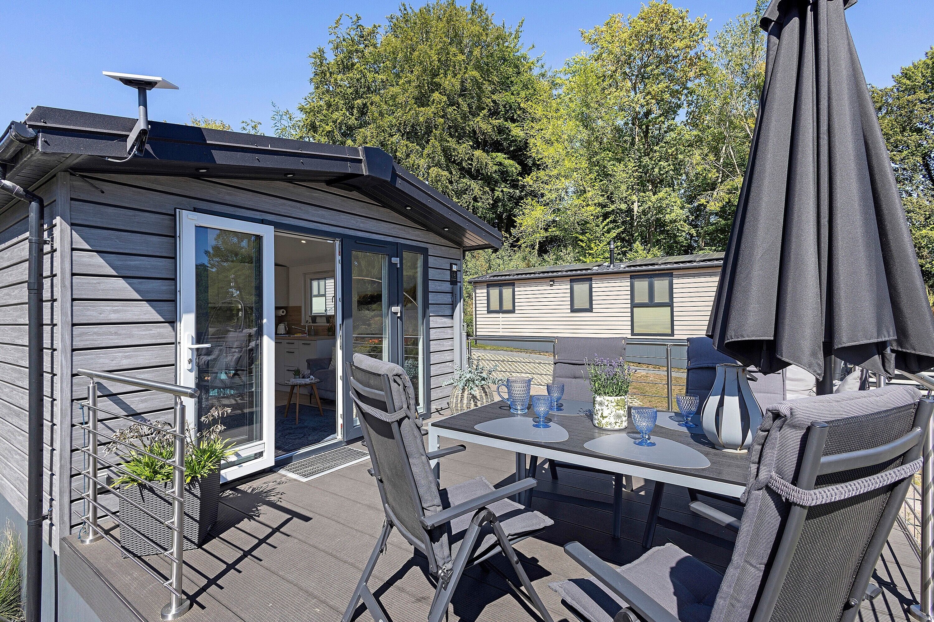 Ein kleines Blockhaus mit einer Terrasse, inklusive Tisch, Stühlen und Sonnenschirm.