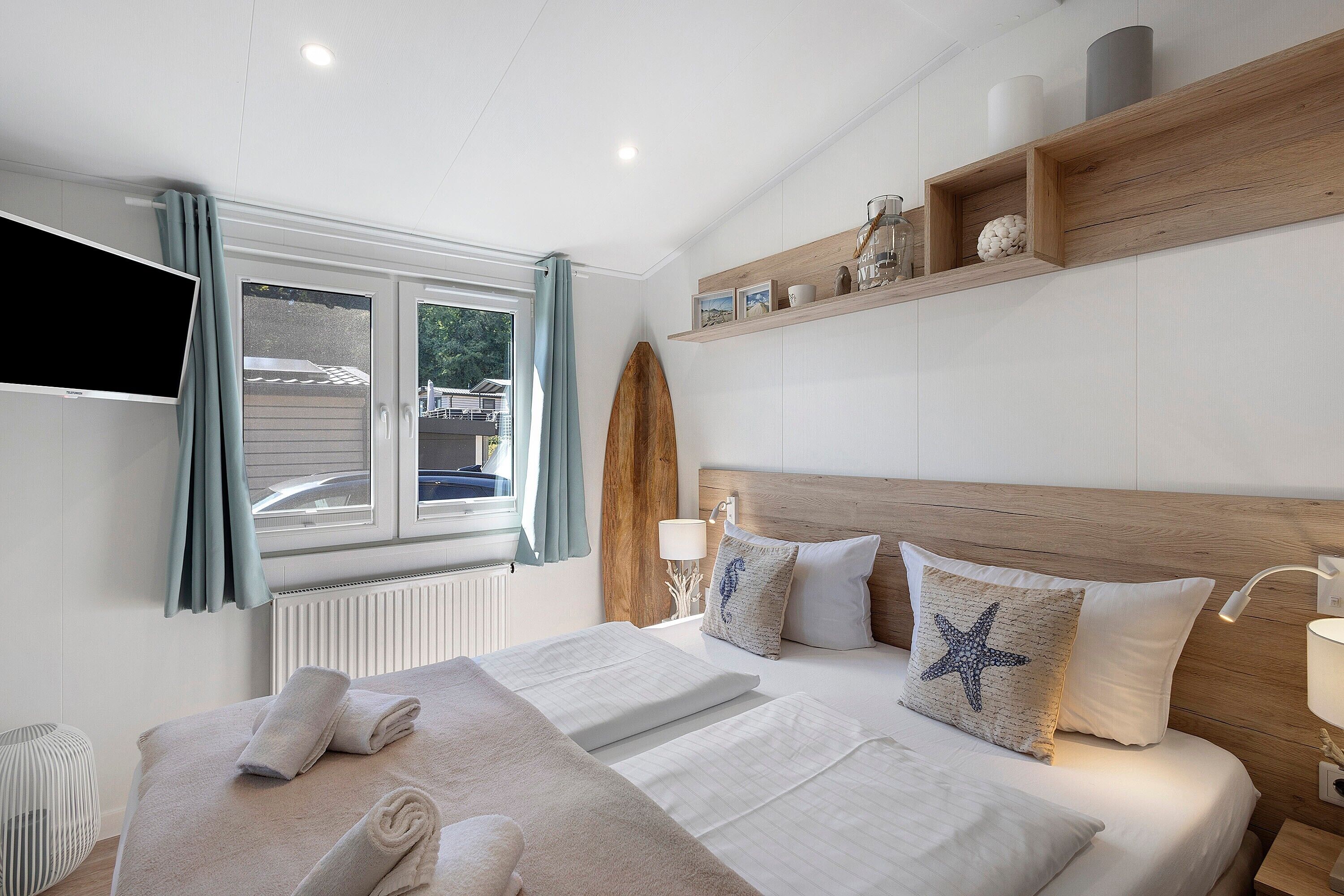 Ein Hotelzimmer mit Bett, Fernseher, einem Fenster mit Vorhängen und einem Holzboden mit Dekoration.