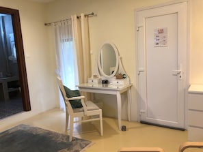 Ein Zimmer mit weißem Schminktisch, einem Stuhl, einer Tür mit einem Notausgangsschild und einem fenster mit Vorhängen.