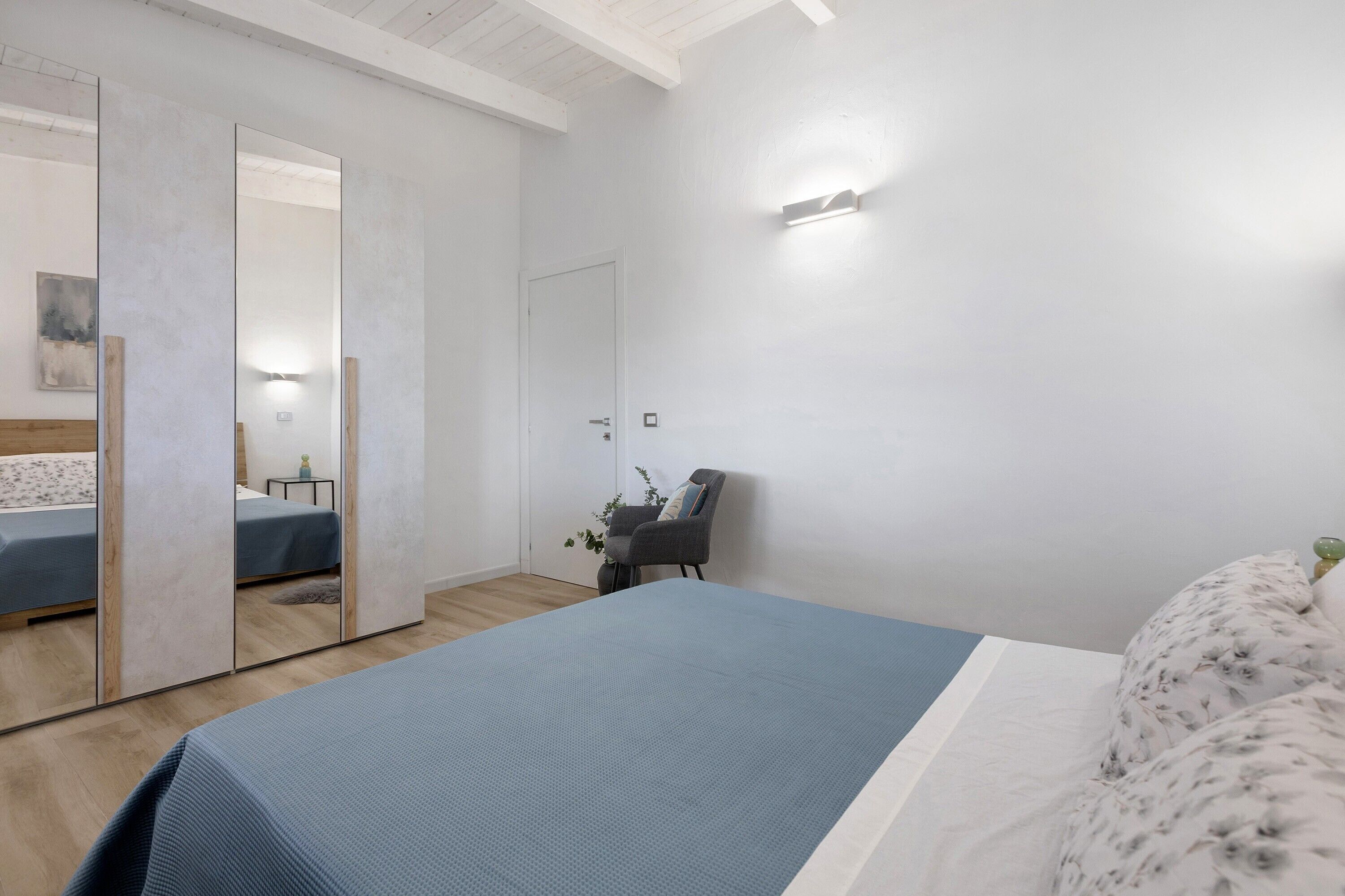 Un dormitorio con una cama, una silla, un espejo y una lámpara de pared.