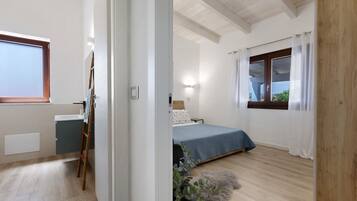Un dormitorio con cama, ventana, mesita de noche y una planta en maceta.
